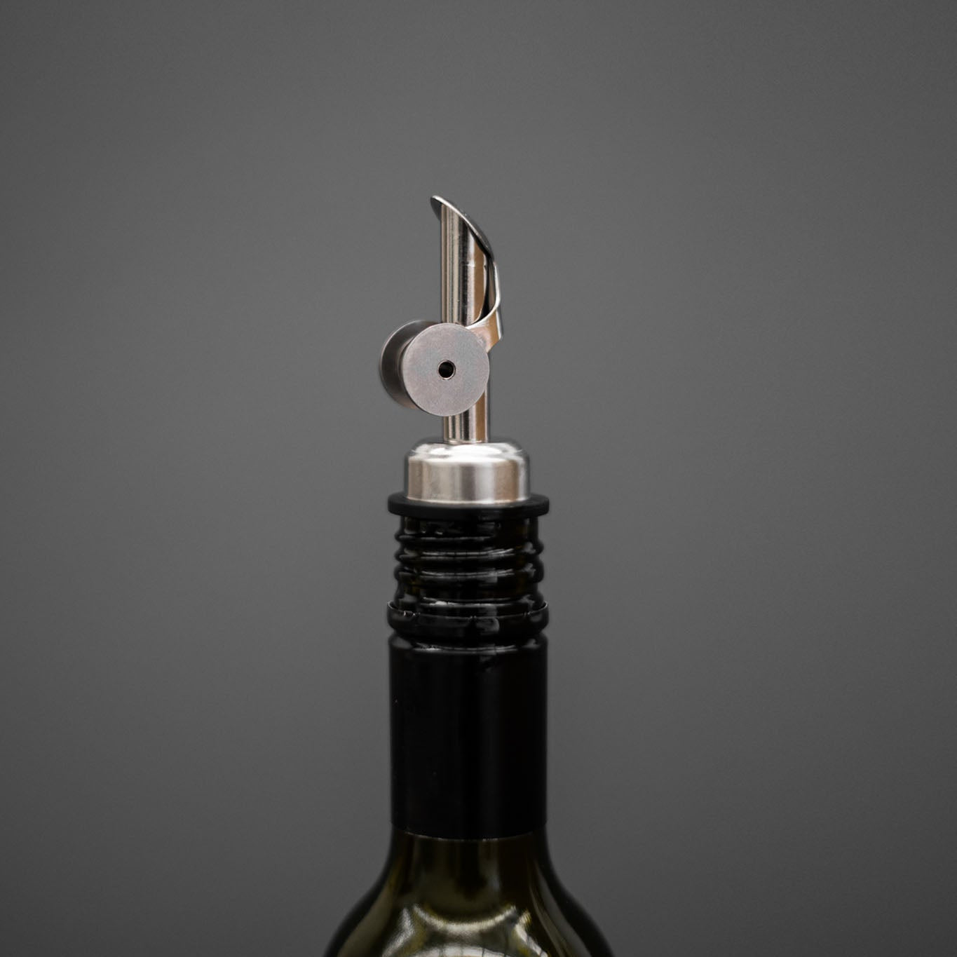 Olive oil pourer on an olive oil bottle against a gray background